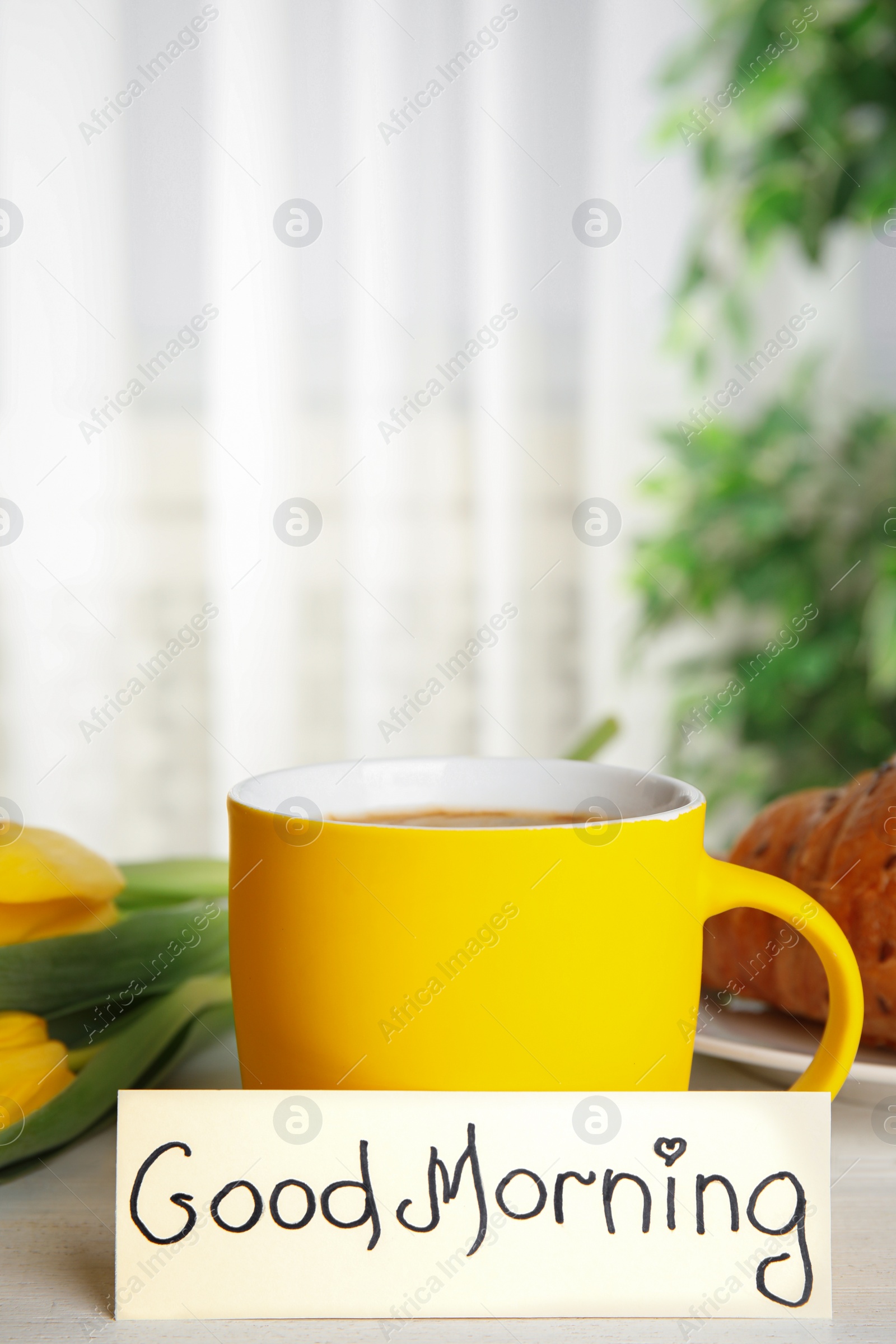 Photo of Croissant, coffee, beautiful flowers and card with words GOOD MORNING on white wooden table indoors