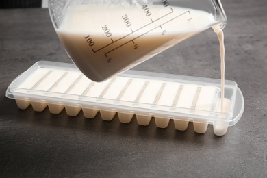 Photo of Pouring milk into ice cube tray on grey table