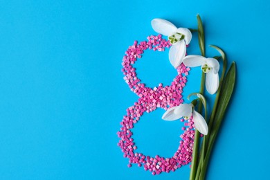 Photo of Beautiful snowdrops and number 8 made of decorative mosaic stones on light blue background, flat lay. Space for text