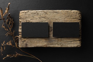 Photo of Empty business cards, piece of wood and dried plant on black background, flat lay. Mockup for design
