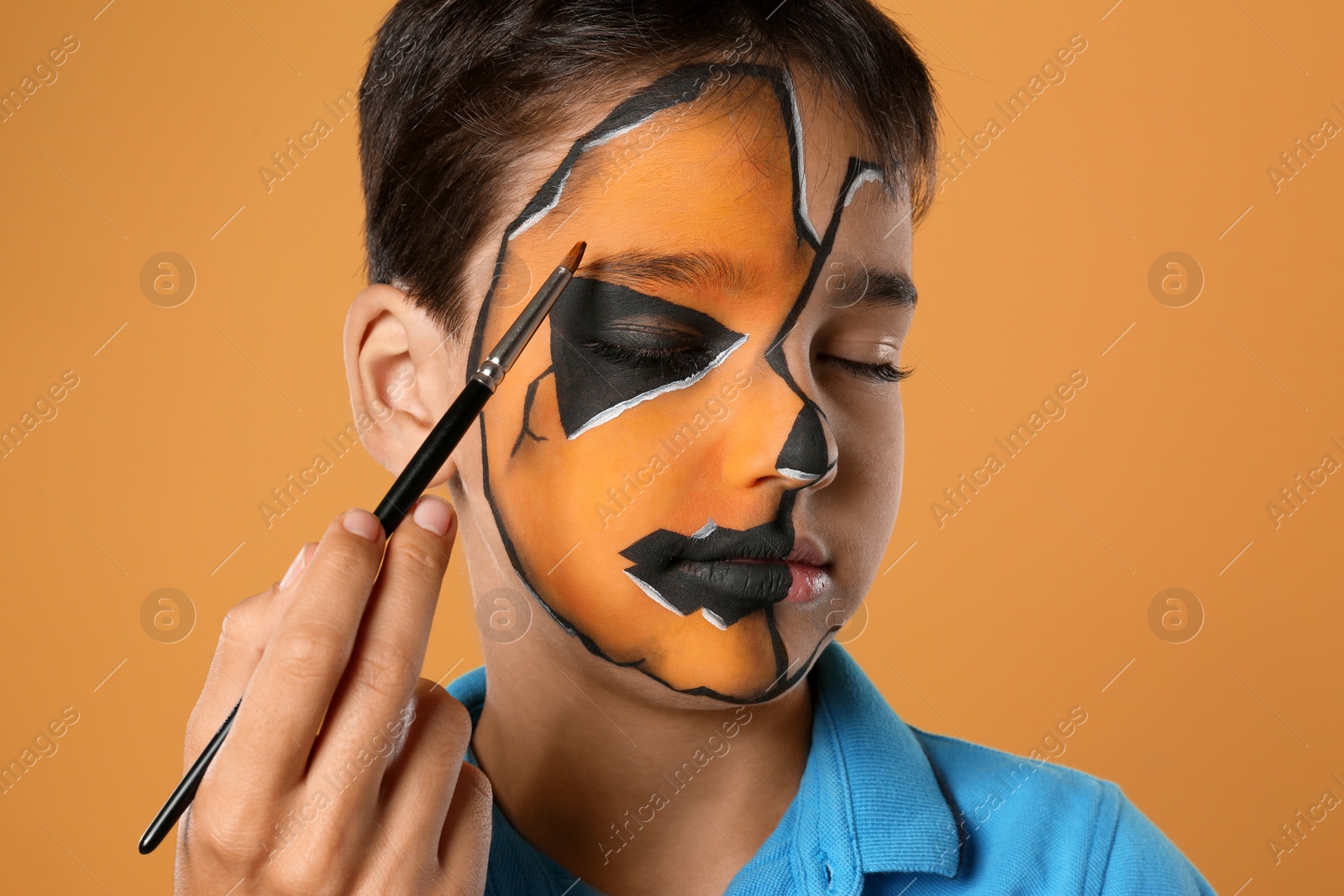 Photo of Artist painting face of little boy on orange background