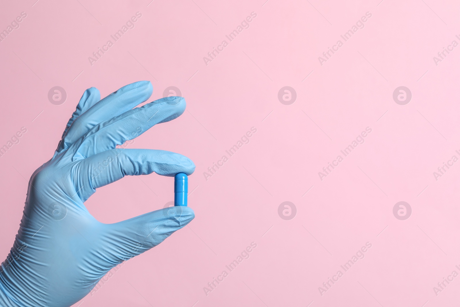 Photo of Doctor holding pill on pink background, closeup. Space for text