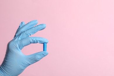 Photo of Doctor holding pill on pink background, closeup. Space for text