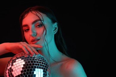 Beautiful woman with disco ball posing in neon lights against black background. Space for text