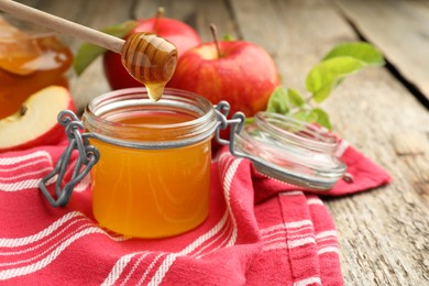 Dripping sweet honey from dipper into jar and fresh apples on wooden table, selective focus. Space for text