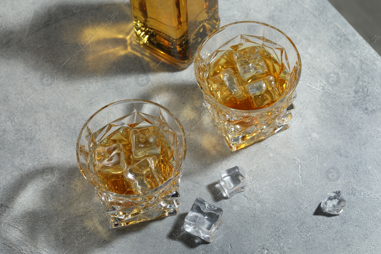 Photo of Whiskey in glasses with ice cubes on grey textured table, above view