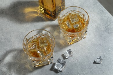 Whiskey in glasses with ice cubes on grey textured table, above view