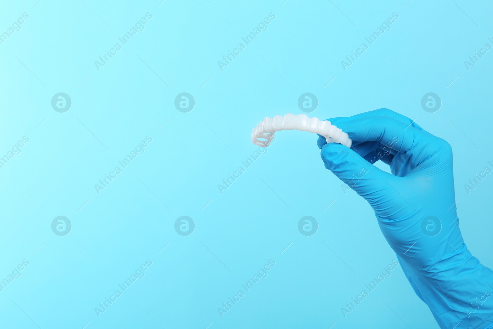 Photo of Dentist holding teeth cover on color background. Space for text