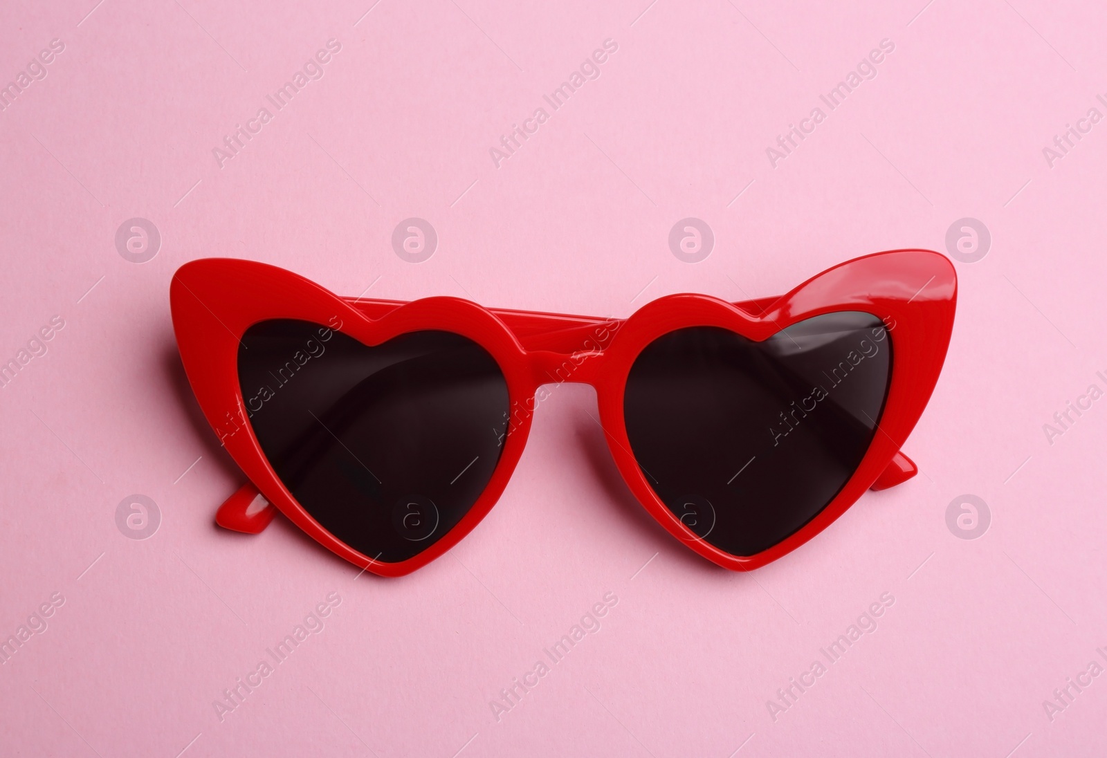 Photo of Stylish heart shaped sunglasses on pink background, top view. Fashionable accessory