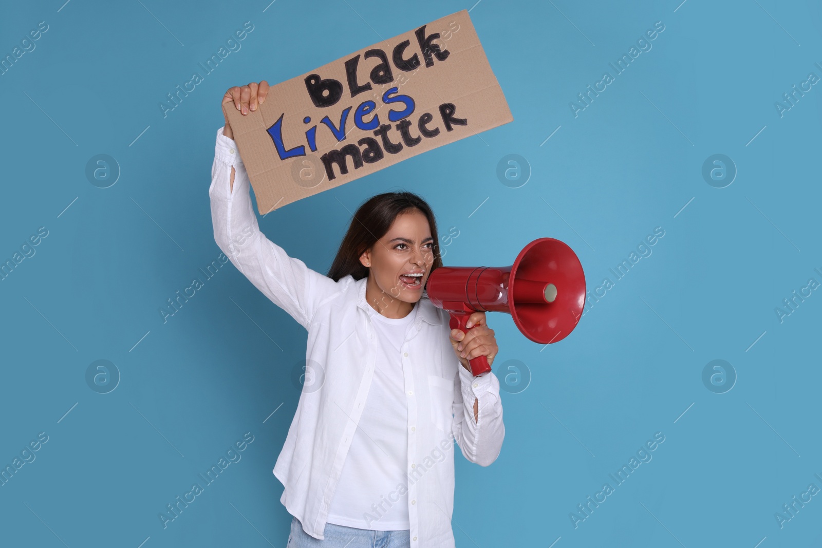 Photo of Emotional woman shouting into megaphone while holding sign with phrase Black Lives Matter on light blue background. End Racism