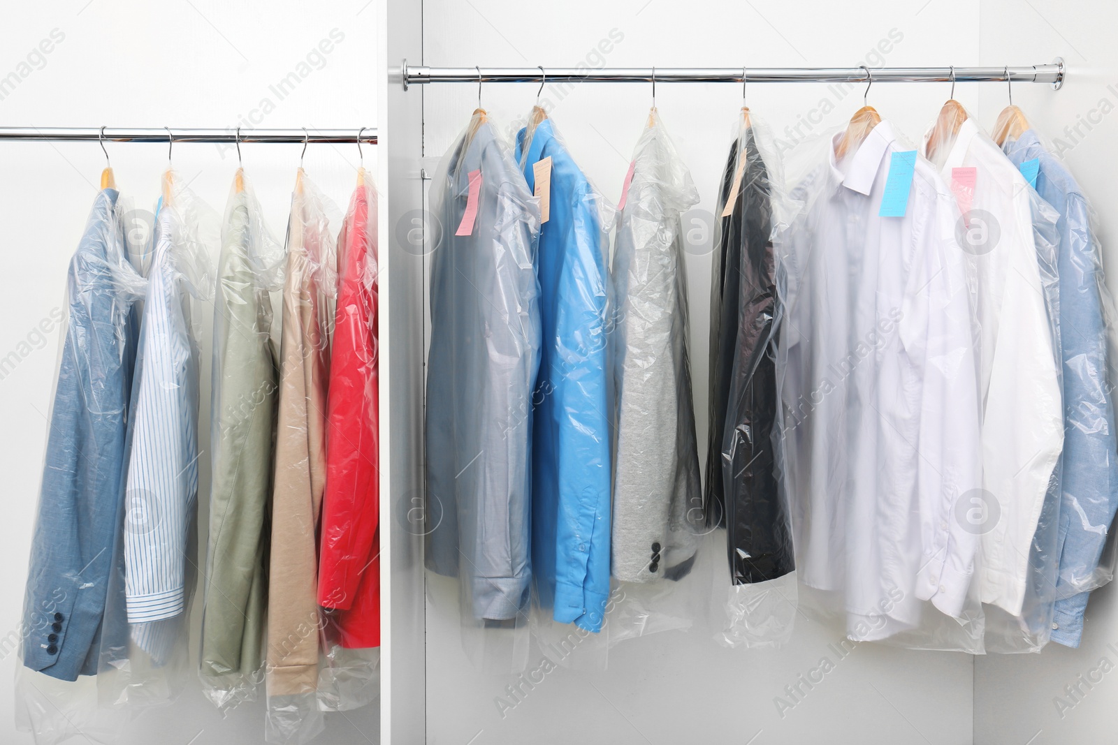 Photo of Racks with clean clothes after dry-cleaning on hangers in wardrobe