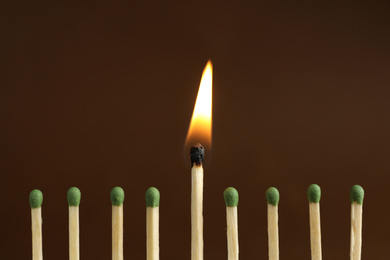 Photo of Burning match among unlit ones on brown background, closeup