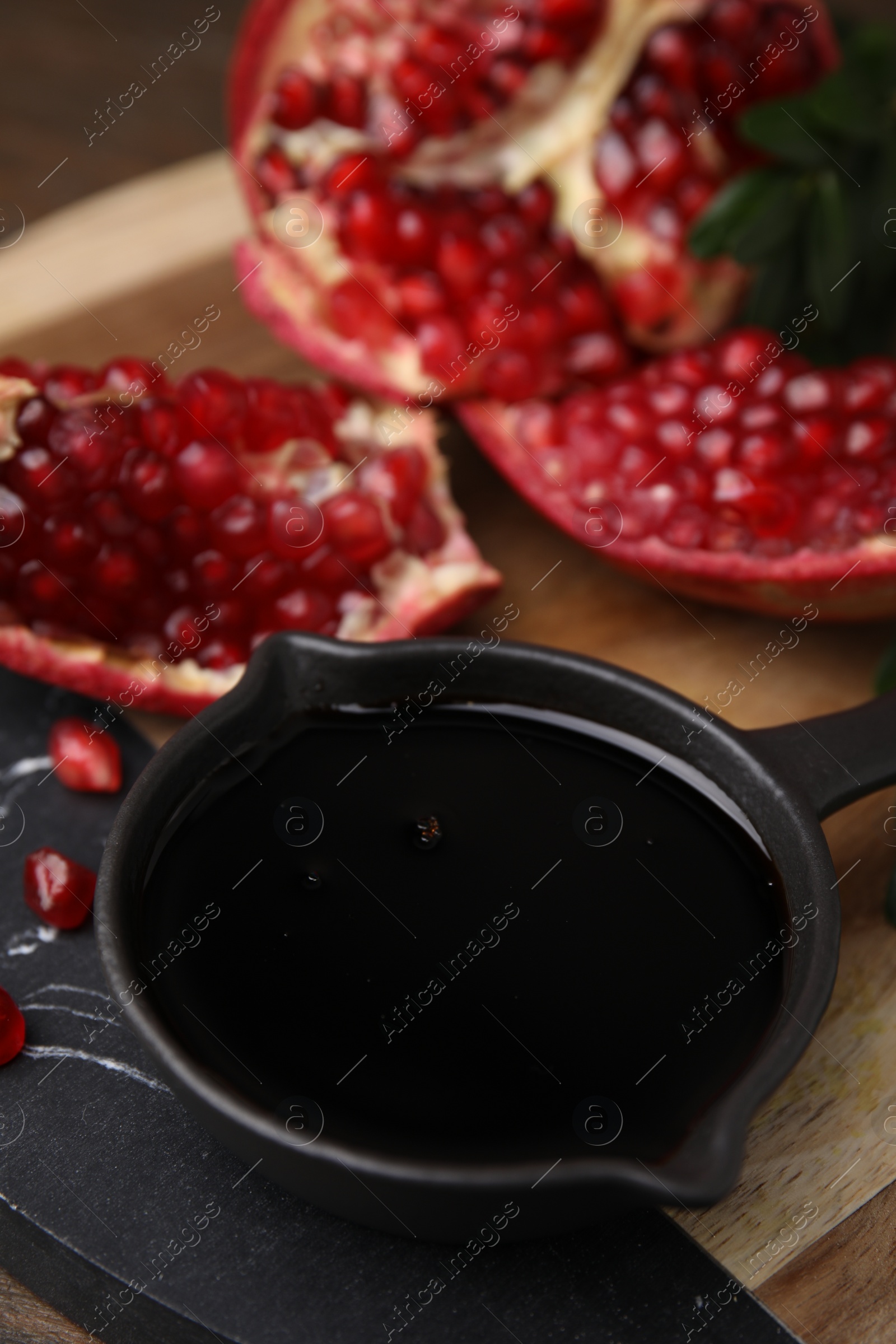 Photo of Tasty pomegranate sauce in bowl and fruit on table, closeup