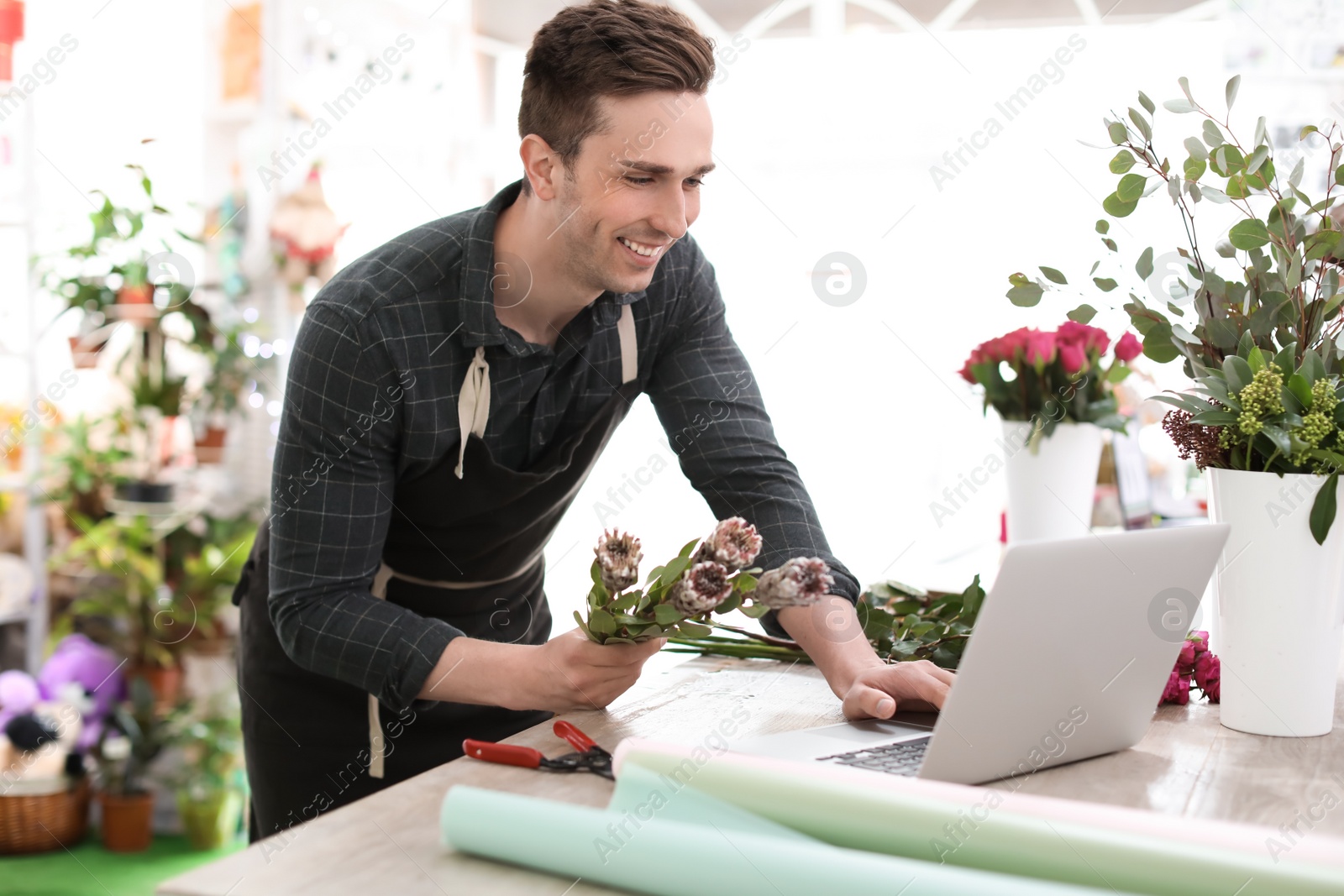 Photo of Young florist working with laptop in flower shop