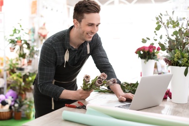 Photo of Young florist working with laptop in flower shop