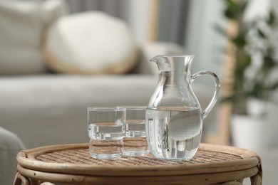 Jug and glass with water on wicker table against blurred background