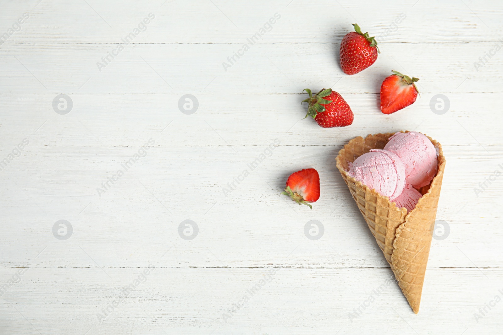 Photo of Delicious ice cream in waffle cone and strawberries on wooden table, space for text