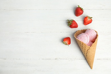 Delicious ice cream in waffle cone and strawberries on wooden table, space for text