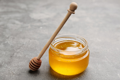 Photo of Tasty honey and wooden dipper on light grey table