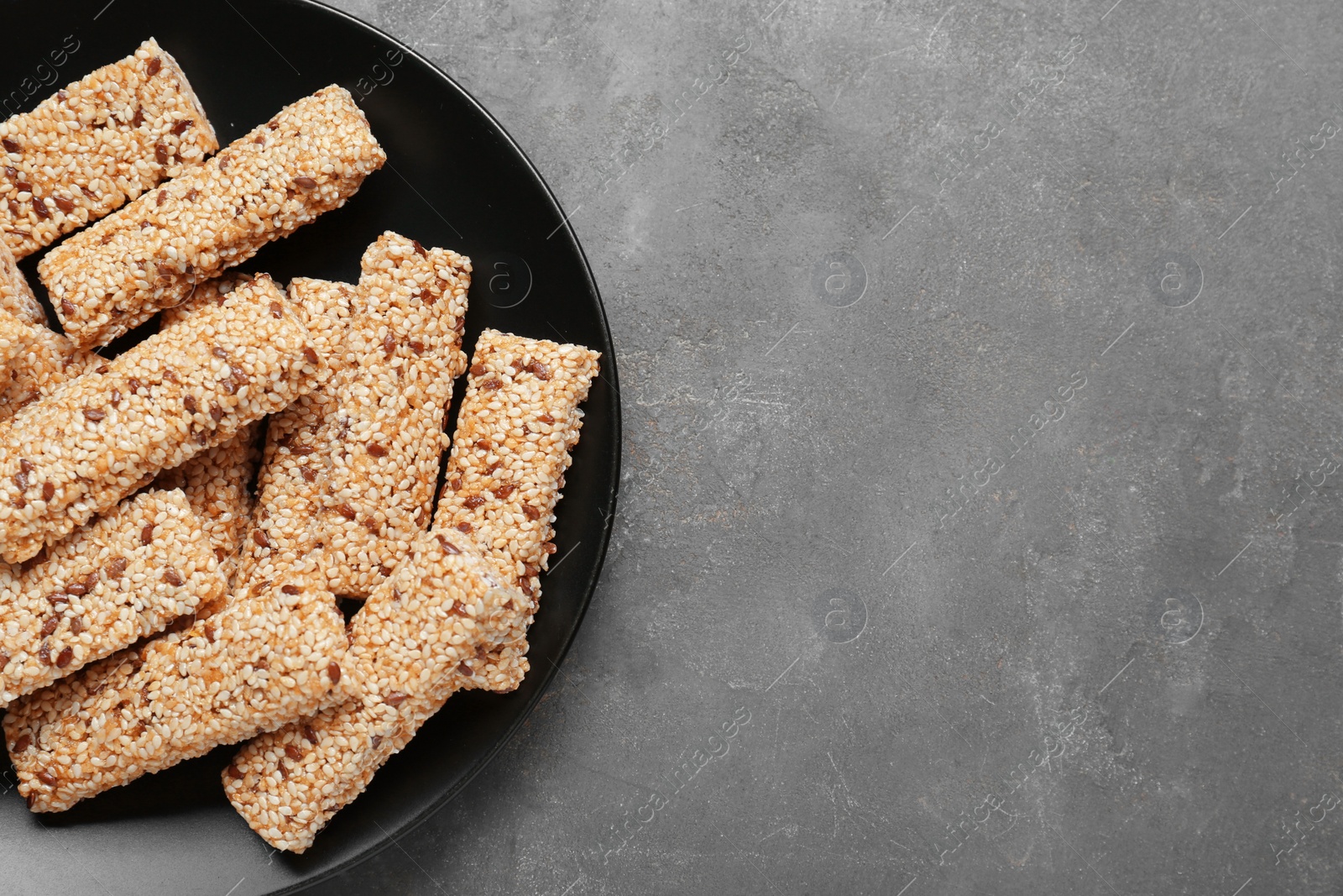 Photo of Plate with tasty sesame seed bars on grey table, top view. Space for text