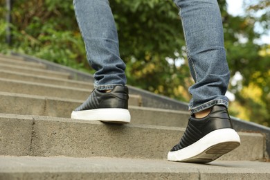 Photo of Man in stylish black sneakers walking up stairs, closeup
