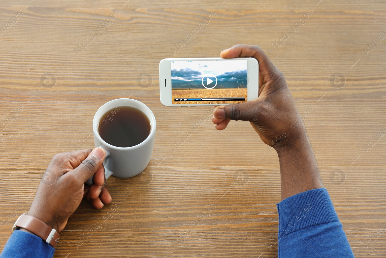 Image of Man watching video on mobile phone while drinking coffee at wooden table, closeup