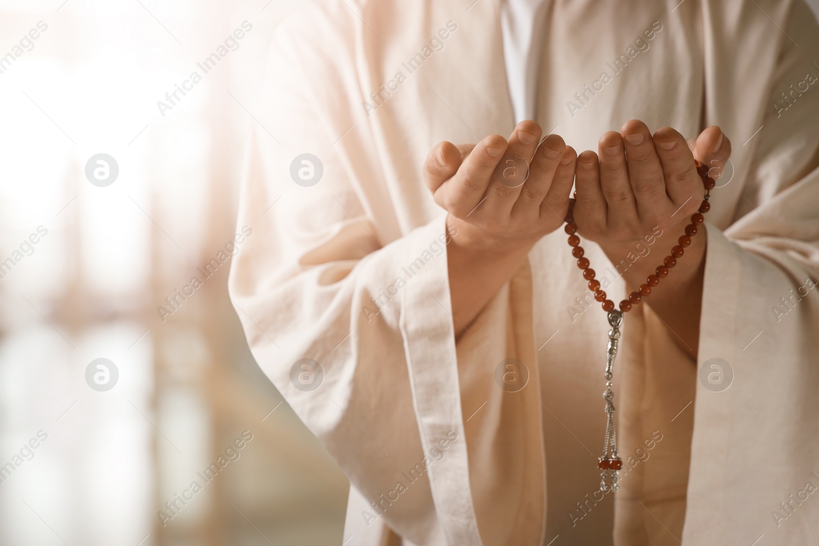 Image of Muslim man with misbaha praying on blurred background, closeup. Space for text