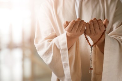 Image of Muslim man with misbaha praying on blurred background, closeup. Space for text