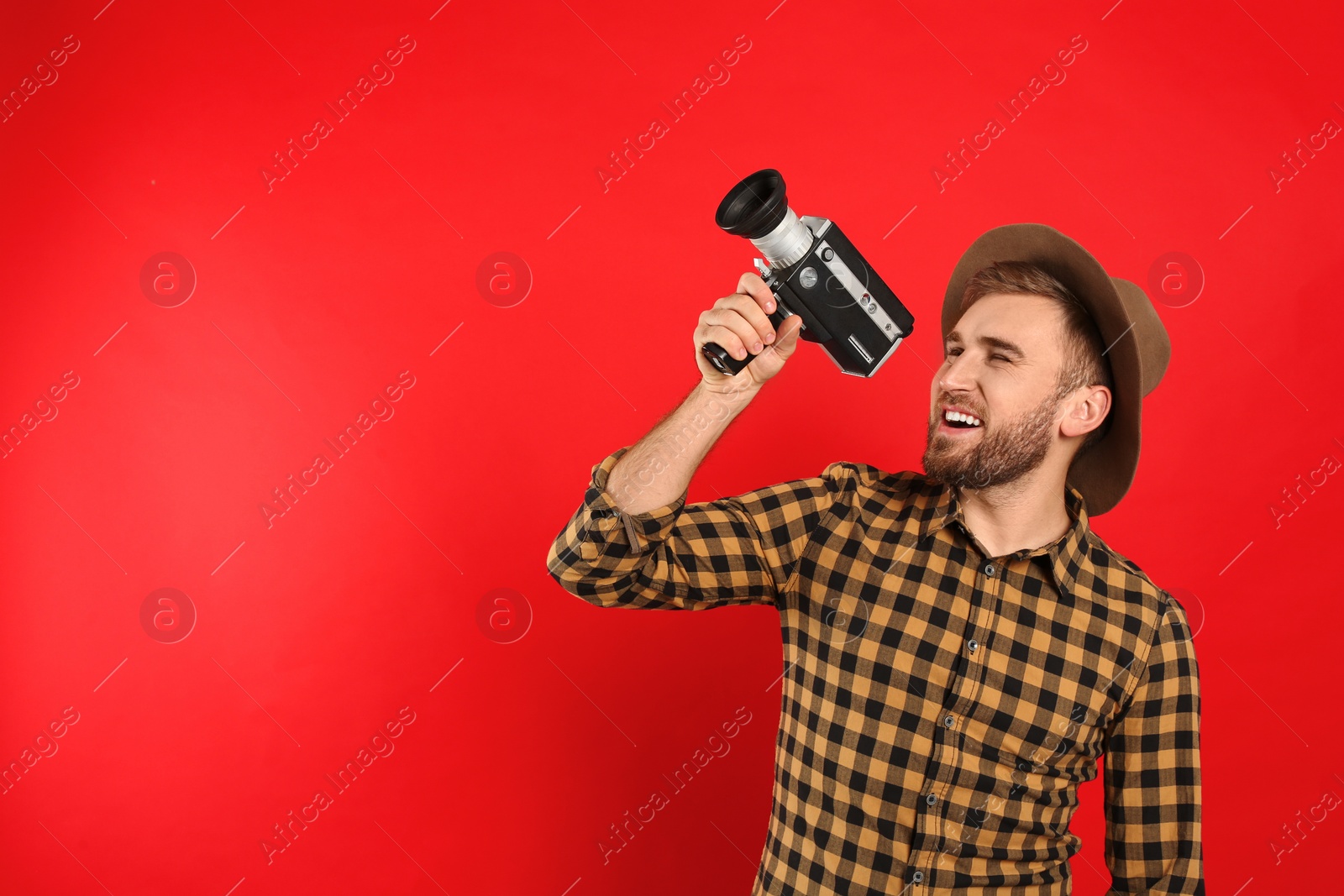 Photo of Young man with vintage video camera on red background. Space for text