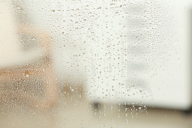 Photo of Blurred view of room through glass with water drops, closeup