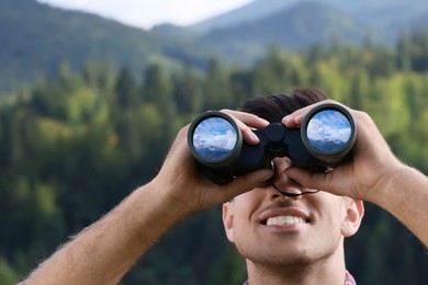 Man looking through binoculars outdoors. Mountain landscape reflecting in lenses