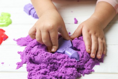 Little child playing with kinetic sand at white wooden table, closeup