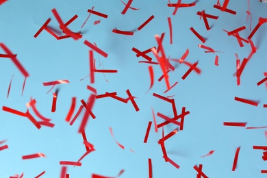 Photo of Shiny red confetti falling down on light blue background