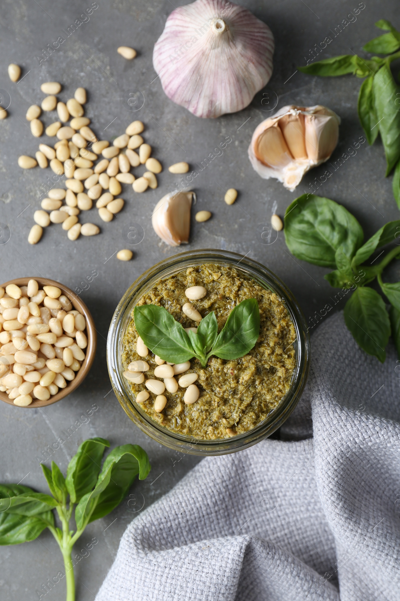 Photo of Jar of delicious pesto sauce and ingredients on grey table, flat lay