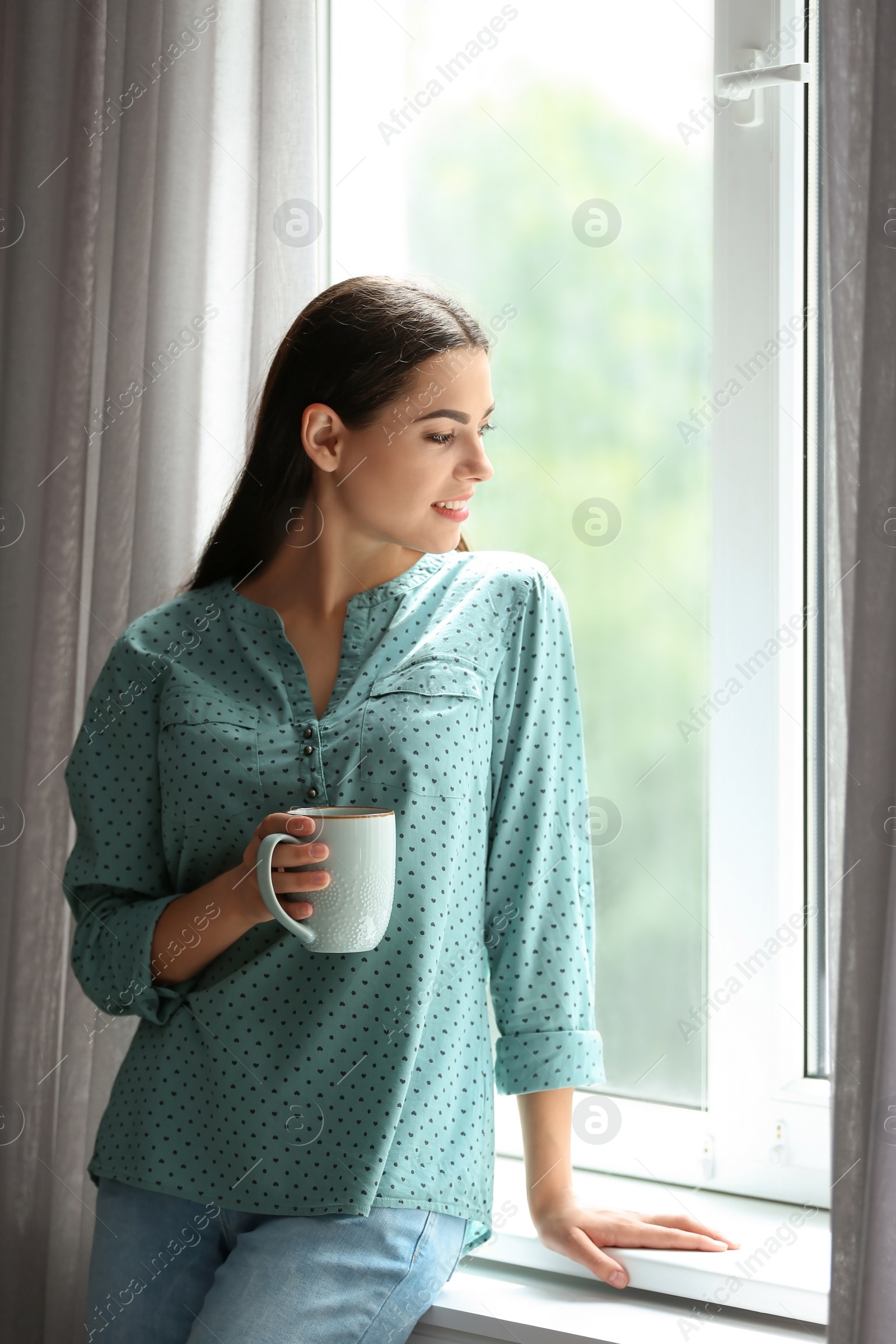 Photo of Young beautiful woman drinking morning coffee near window at home