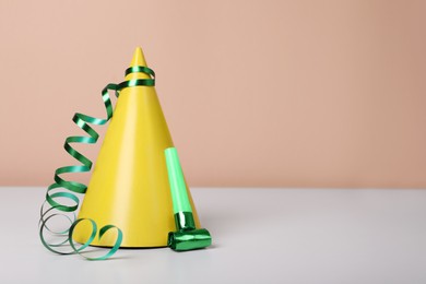 Photo of Colorful party hat, streamer and blower on white table, space for text. Birthday celebration