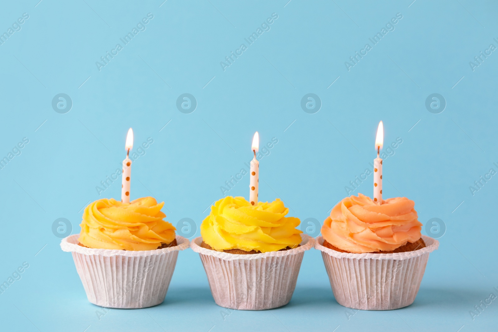 Photo of Tasty birthday cupcakes with candles on light blue background. Space for text