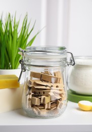 Photo of Many wooden clothespins in glass jar on white table