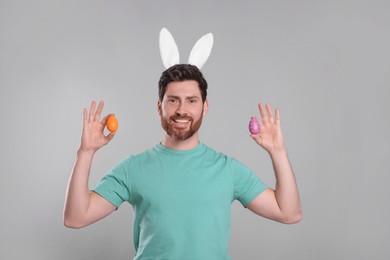 Portrait of happy man in cute bunny ears headband holding Easter eggs on light grey background
