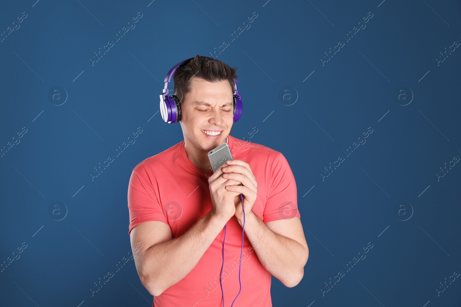 Photo of Man in headphones with mobile device on color background. Space for text