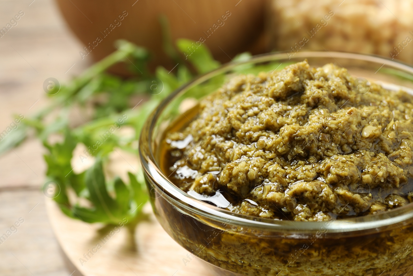 Photo of Bowl of tasty arugula pesto on table, closeup