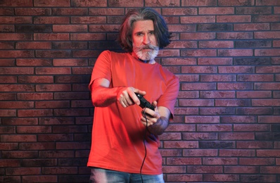 Emotional mature man playing video games with controller near brick wall