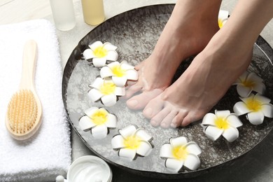 Photo of Woman soaking her feet in bowl with water and flowers on floor, closeup. Spa treatment