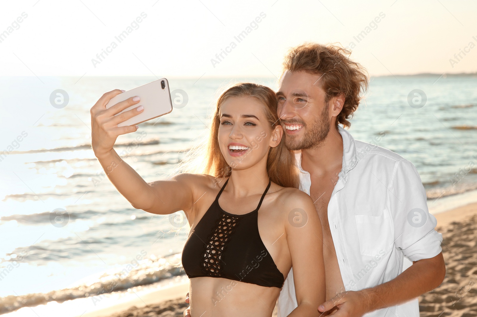 Photo of Happy young couple in beachwear taking selfie on seashore