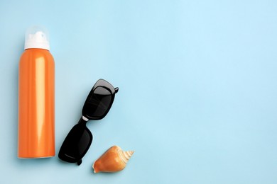 Bottle of sunscreen, sunglasses and seashell on light blue background, flat lay. Space for text