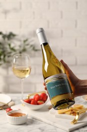 Woman holding bottle of wine over table with different snacks, closeup