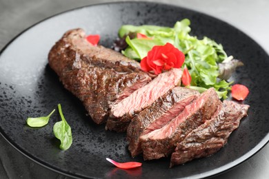 Pieces of delicious grilled beef meat and greens on table, closeup