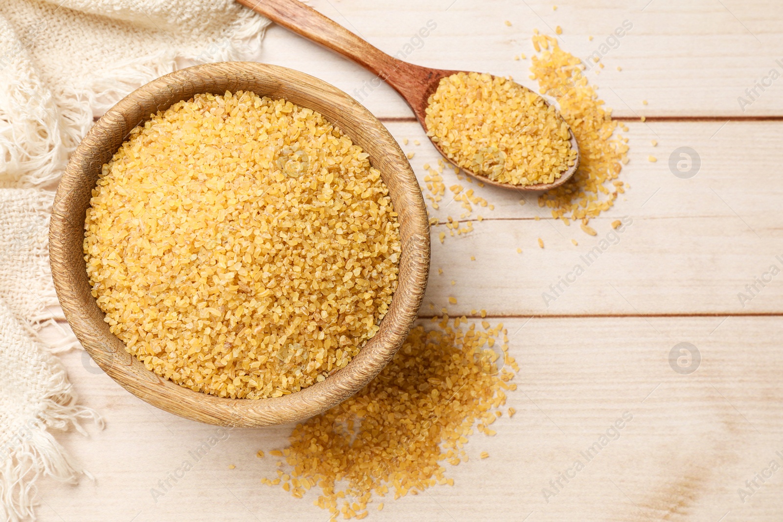 Photo of Bowl and spoon with raw bulgur on light wooden table, top view. Space for text