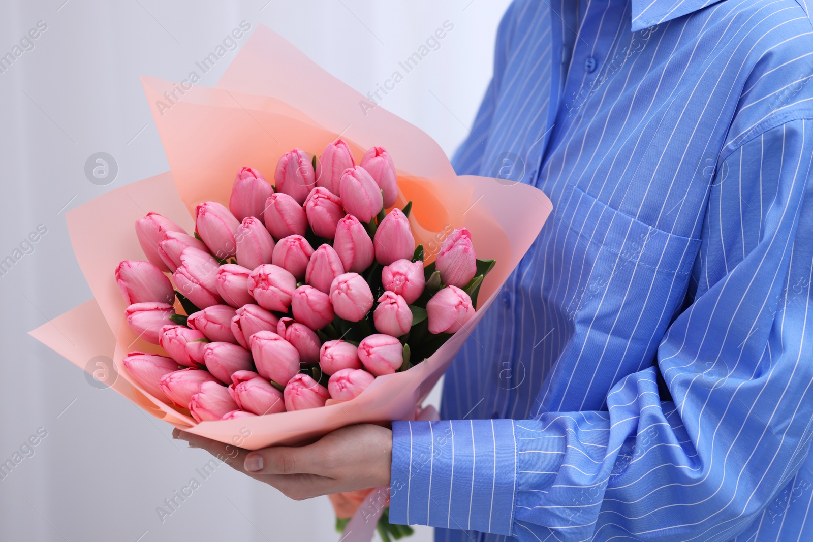 Photo of Woman holding bouquet of pink tulips indoors, closeup