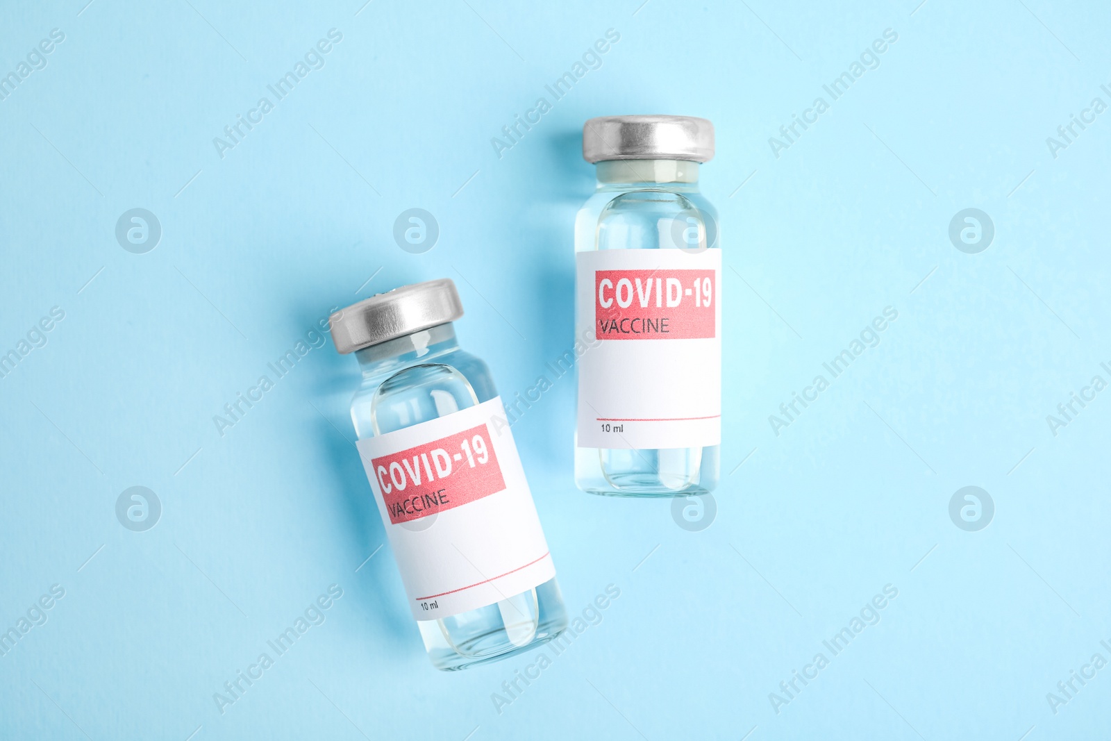 Photo of Vials with coronavirus vaccine on light blue background, flat lay